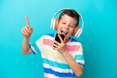 Küçük çocuk mavi arka planda izole edilmiş, müzik dinliyor ve şarkı söylüyor.