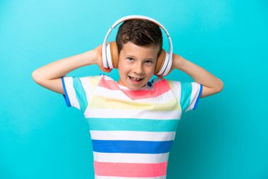 Küçük çocuk mavi arka planda izole edilmiş müzik dinliyor.