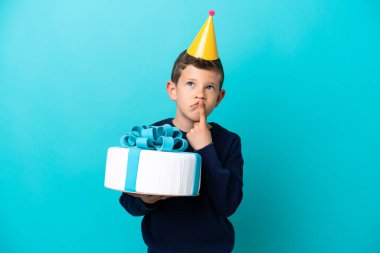 Küçük çocuk mavi arka planda izole edilmiş doğum günü pastası tutuyor.