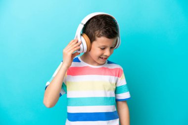Küçük çocuk mavi arka planda izole edilmiş müzik dinliyor.