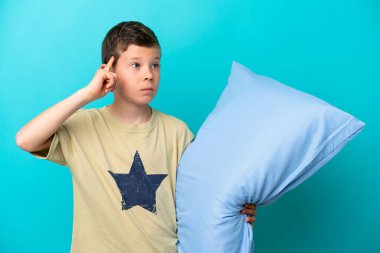 Mavi arka planda izole edilmiş pijamalı küçük bir çocuğun şüpheleri ve düşünceleri var.