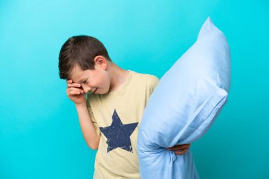 Pijamalı küçük çocuk mavi arka planda yalnız gülüyor.