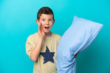 Pijamalı küçük bir çocuk mavi arka planda izole edilmiş, şaşırmış ve şok olmuş bir yüz ifadesi var.