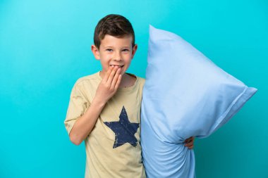 Mavi arka planda izole edilmiş pijamalı küçük çocuk mutlu ve gülümsüyor.