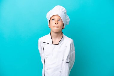 Küçük aşçı çocuk mavi arka planda izole edilmiş ve yukarı bakıyor.