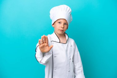 Mavi arka planda izole edilmiş küçük aşçı çocuk dur hareketi yapıyor.