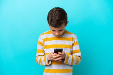 Küçük çocuk mavi arka planda cep telefonu kullanarak izole edilmiş.