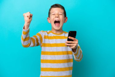 Küçük çocuk mavi arka planda cep telefonu kullanarak ve zafer jesti yaparak izole edildi.