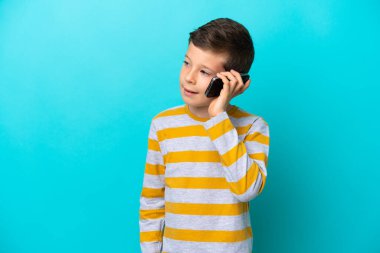 Küçük çocuk mavi arka planda izole edilmiş. Cep telefonuyla biriyle sohbet ediyor.