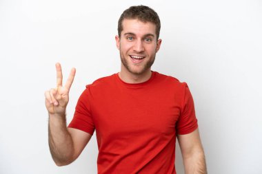 Beyaz arka planda izole edilmiş genç beyaz adam gülümsüyor ve zafer işareti gösteriyor.