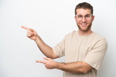 Beyaz arka planda izole edilmiş beyaz tenli genç adam parmağını yana doğru uzattı ve bir ürün sundu.