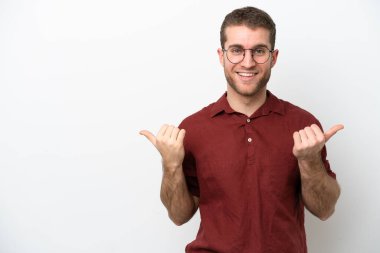 Beyaz arka planda izole edilmiş genç beyaz bir adam. Baş parmakları havada ve gülümsüyor.