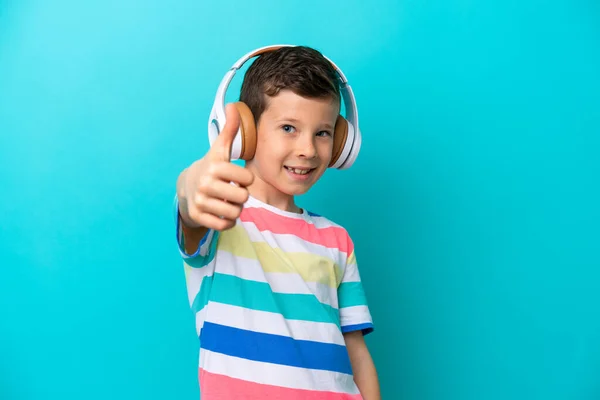 小男孩被蓝色背景隔离在一边 一边听着音乐 一边竖起大拇指 — 图库照片