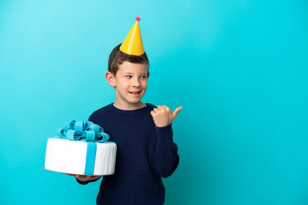 Menino Segurando Bolo Aniversário Isolado Fundo Azul Apontando Para Lado — Fotografia de Stock