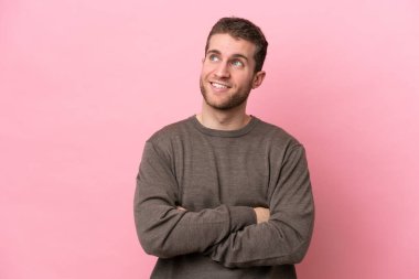 Pembe arka planda izole edilmiş genç beyaz adam gülümserken yukarı bakıyor.