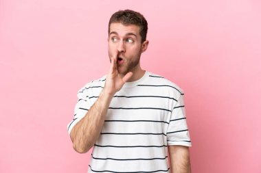 Pembe arka planda izole edilmiş genç beyaz adam yan tarafa bakarken sürpriz bir jest yapıyor.