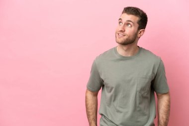 Kafkasyalı genç bir adam pembe arka planda izole edilmiş, yukarı bakarken bir fikir düşünüyor.