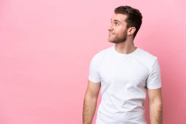 Pembe arka planda izole edilmiş genç beyaz adam yana bakıyor ve gülümsüyor.