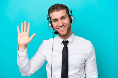 Telemarketer caucasian man working with a headset isolated on blue background saluting with hand with happy expression