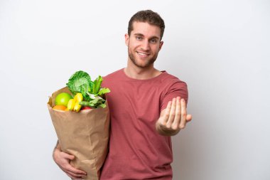 Beyaz arka planda izole edilmiş alışveriş torbası tutan genç beyaz bir adam bizimle gelmesi için davet ediyor. Gelmene sevindim.