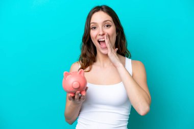 Beyaz bir kadın elinde kumbarayla mavi bir fırında izole edilmiş bir şekilde ağzı açık bağırıyor.