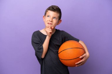 Mor arka planda basketbol oynayan küçük çocuk yukarı bakıyor.