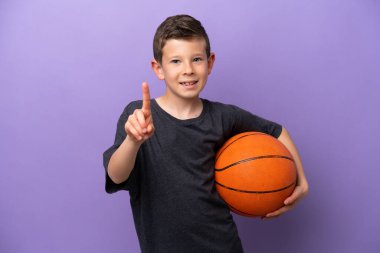 Mor arka planda izole edilmiş basketbol oynayan küçük çocuk parmağını kaldırıyor ve gösteriyor.