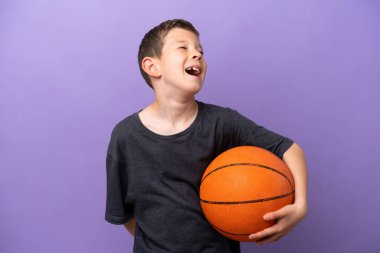 Mor arka planda izole edilmiş basketbol oynayan küçük çocuk gülüyor.