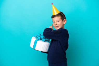 Küçük çocuk elinde doğum günü pastası tutarken mavi arka planda izole edilmiş.
