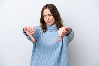 Beyaz arka planda izole edilmiş genç beyaz kadın baş parmağını iki eliyle aşağı gösteriyor.