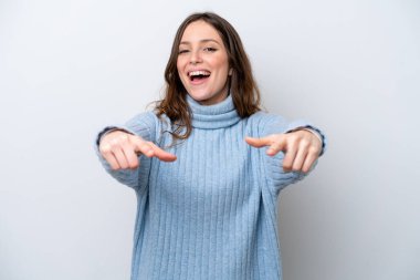 Beyaz arka planda izole edilmiş genç beyaz kadın şaşırmış ve ön tarafı işaret ediyor.