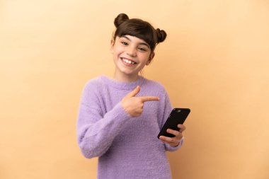 Küçük beyaz kız bej arka planda izole edilmiş ve cep telefonu kullanıyor.