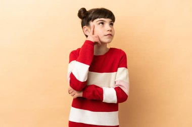 Kafkasyalı küçük bir kız bej arka planda izole edilmiş bir fikir düşünüyor.