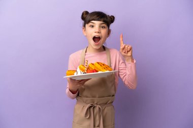 Mor arka planda izole edilmiş waffle 'lar tutan küçük beyaz kız bir fikir düşünüyor.