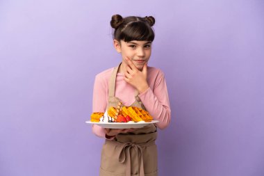 Mor arka planda izole edilmiş waffle tutan küçük beyaz kız.