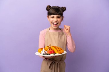 Mor arka planda gözleme tutan küçük beyaz kız galibiyeti kutluyor.