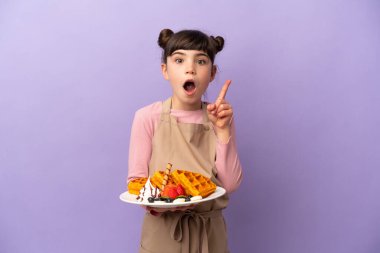 Mor arka planda izole edilmiş waffle 'lar tutan küçük beyaz kız çözümü bulmak için parmağını kaldırıyor.