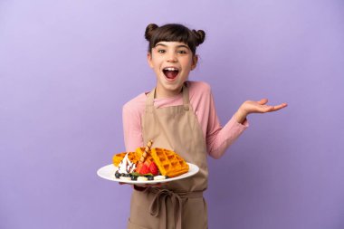 Küçük beyaz kız elinde waffle tutarken mor arka planda şok olmuş yüz ifadesi ile izole edilmiş.