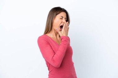 Beyaz arka planda izole edilmiş orta yaşlı beyaz bir kadın esniyor ve ağzını eliyle açık tutuyor.