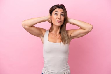 Pembe arka planda izole edilmiş orta yaşlı beyaz kadın hayal kırıklığına uğramış ve kulaklarını kapatmış.