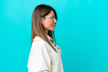 Mavi arka planda gözlüklü, orta yaşlı, beyaz bir kadın.