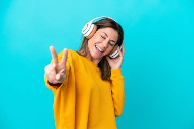 Orta yaşlı beyaz kadın, mavi arka planda izole edilmiş müzik dinliyor ve şarkı söylüyor.