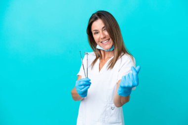 Orta yaşlı dişçi kadının elinde mavi arka planda izole edilmiş aletler var.