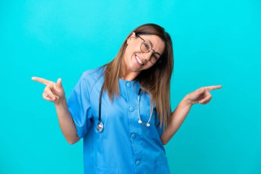 Mavi arka planda izole edilmiş orta yaşlı cerrah kadın parmak uçlarında ve mutlu.