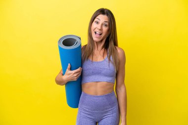 Elinde paspas tutarken yoga derslerine giden sporcu kadın sürpriz bir yüz ifadesi ile sarı olmayan bir zemin tutuyor.