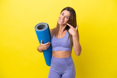 Elinde paspas tutarken yoga derslerine giden spor kadını sarı olmayan bir arkaplanda baş parmak işareti yapıyor.