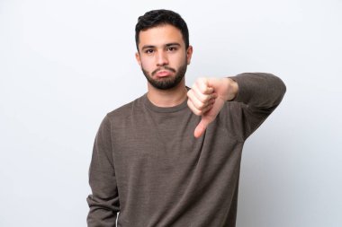 Beyaz arka planda izole edilmiş genç Brezilyalı adam olumsuz ifadeyle baş parmağını aşağı gösteriyor.