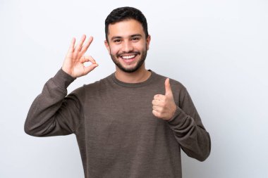 Beyaz arka planda izole edilmiş genç Brezilyalı adam işaret ve baş parmak hareketi gösteriyor.
