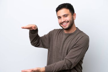 Beyaz arka planda izole edilmiş genç Brezilyalı bir adam bir ilan vermek için kopyalama alanı tutuyor