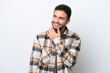 Genç Brezilyalı adam beyaz arka planda izole edilmiş gülümserken yukarı bakıyor